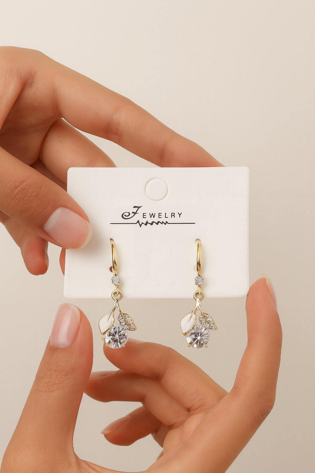 Gold and silver teardrop earrings on a jewelry card held by a hand against a beige background
