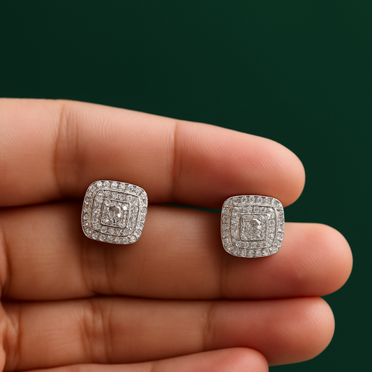 Silver square earrings with gemstones held between fingers against a dark green background