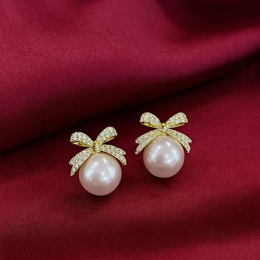 Pearl earrings with gold bows on a red fabric background