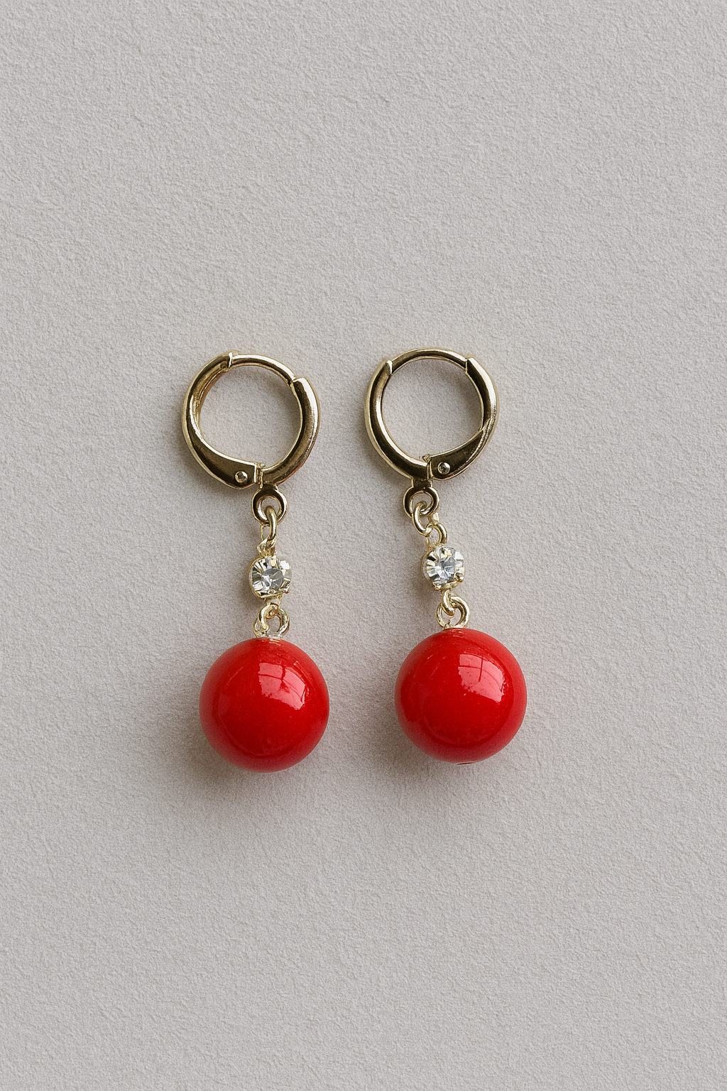 Pair of red ball earrings with gold loops on a light gray background