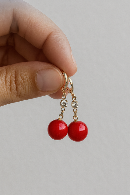 Red earrings with gold hooks held by a hand against a light background