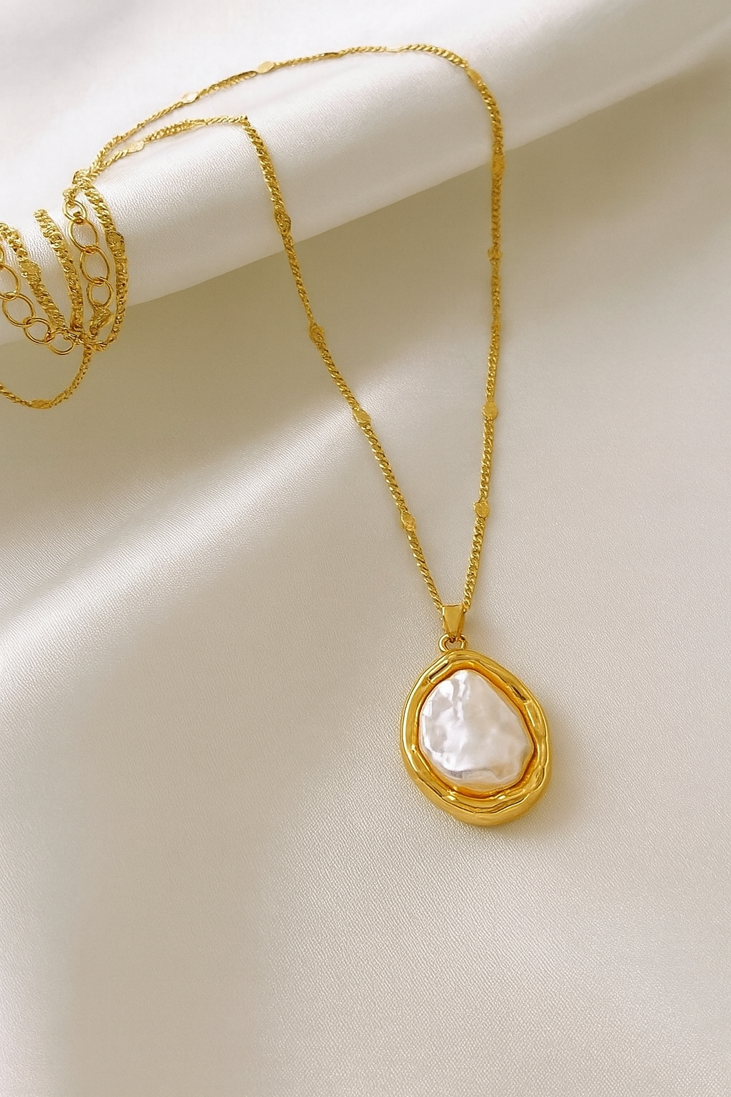 Gold necklace with a teardrop-shaped pendant on a beige background