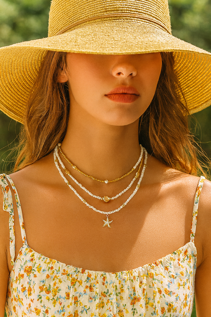 Woman wearing a yellow sun hat and floral dress with layered necklaces.