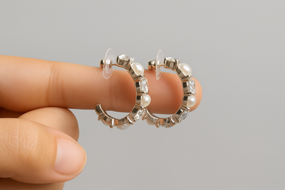 Silver hoop earrings with clear gemstones held between fingers against a gray background