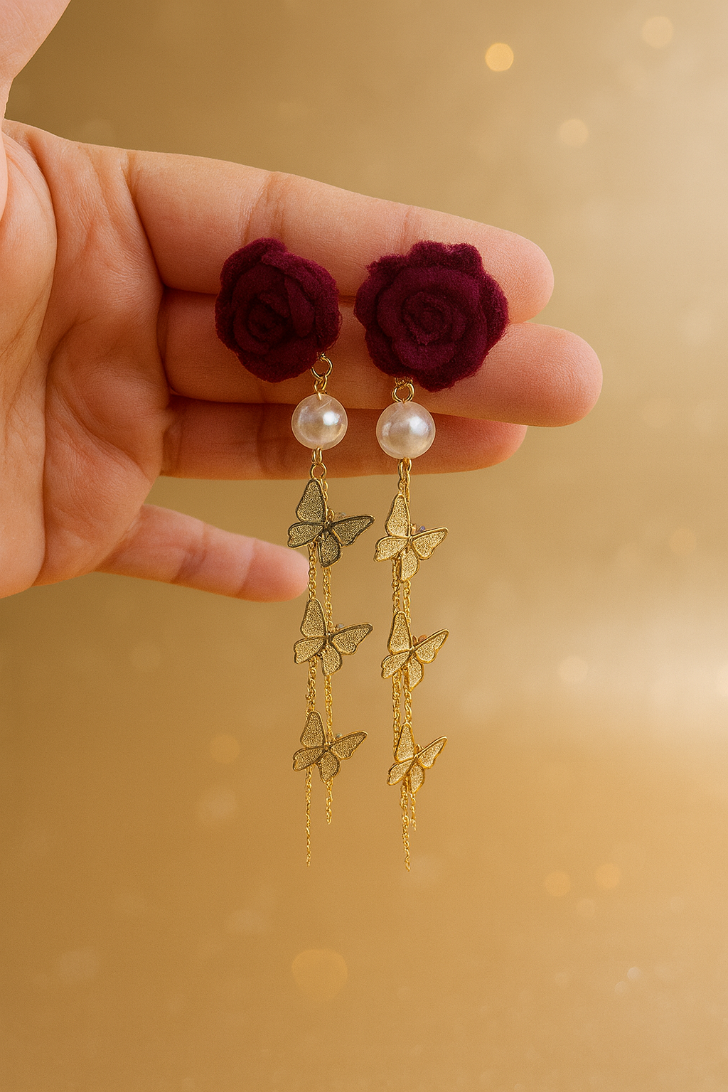 Gold butterfly earrings with maroon flowers held in a hand against a gold background