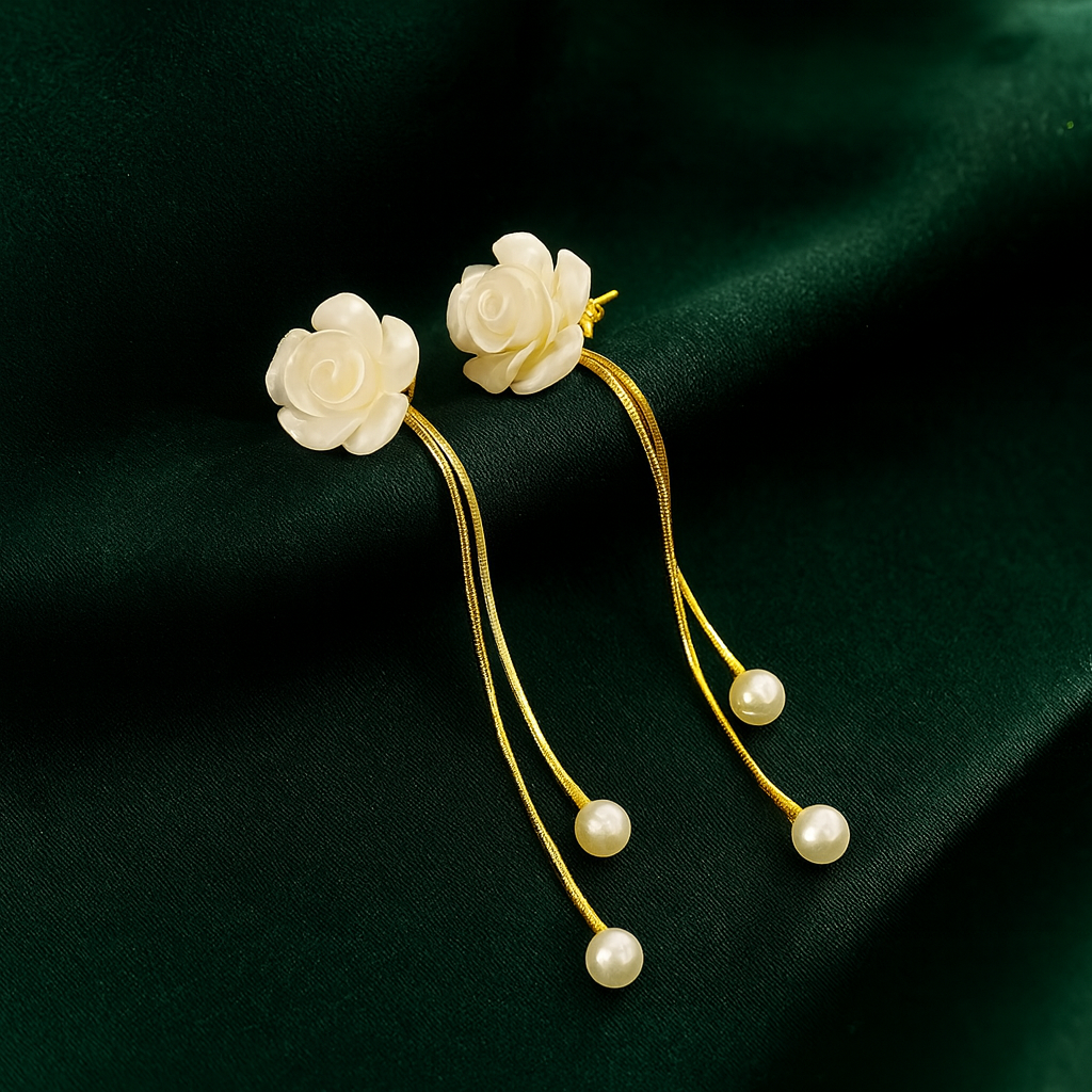 Pair of floral earrings with gold accents and pearl drops on a dark green fabric background