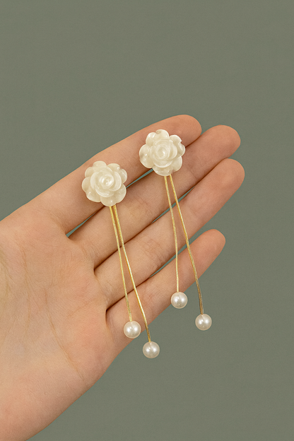 Hand holding a pair of floral hairpins with pearl details against a gray background